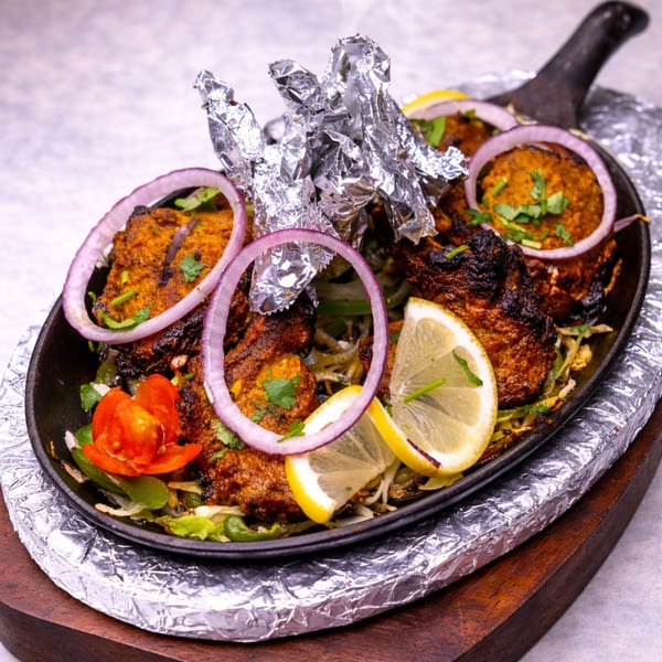 Sizzling Indian tandoori chicken with onions, lemons, and foil-wrapped drumsticks in a cast-iron pan.