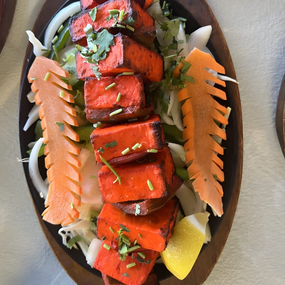 Desi Tadka's paneer tikka, red marinated cheese cubes with carved carrots, onions, and lemon.