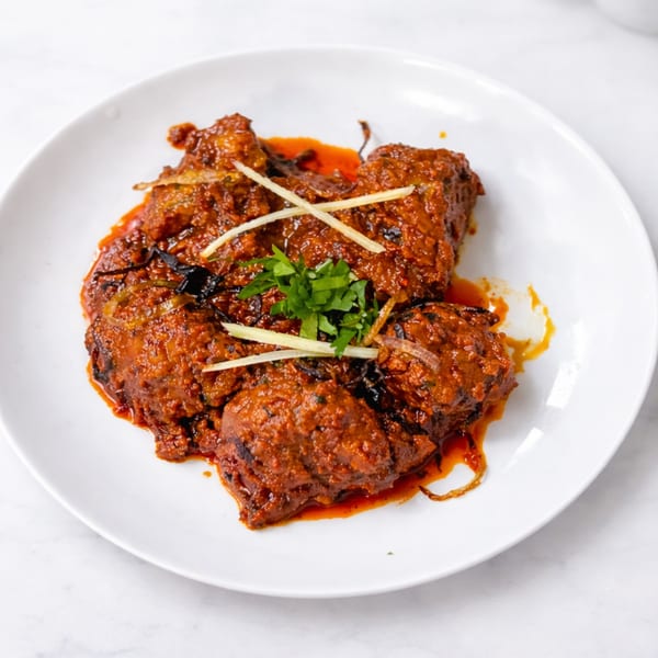 Spicy chicken karahi, garnished with fresh ginger and cilantro, served on a white plate.